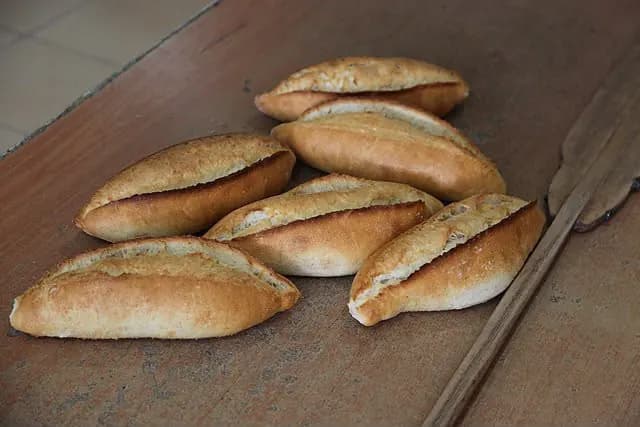 Frisch gebackene türkische Weißbrote mit aufgerissener Kruste auf einem Holzbrett.