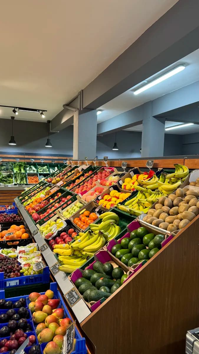 Obst- und Gemüseauslage mit Bananen, Avocados, Trauben und Kiwis in Holzkisten.