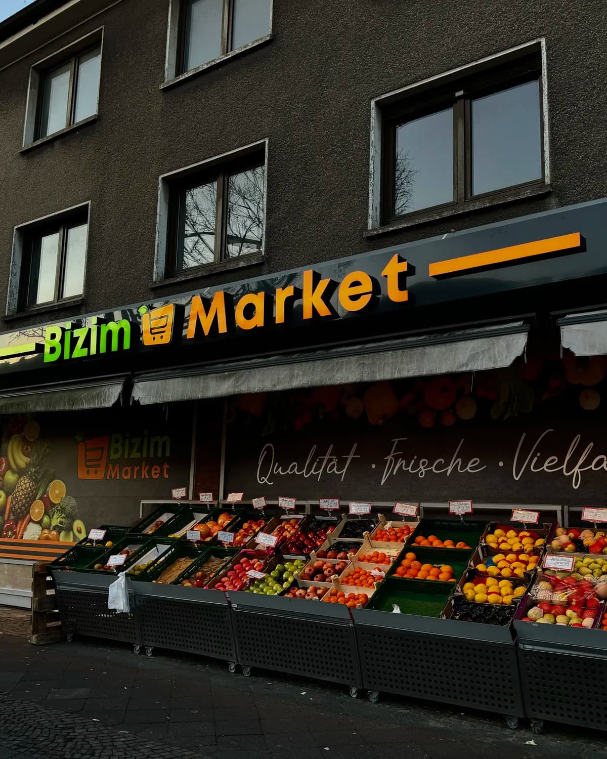 Ladenfront am Abend: Leuchtschrift Bizim Market über der Obstauslage.
